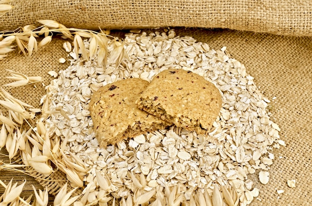 The two halves of biscuits made from oats and berries on a pile of oatmeal, oat stalks on burlap and wooden board