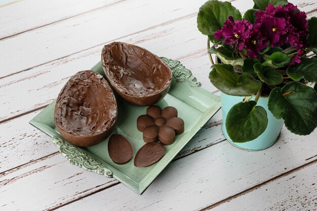 Two halves of chocolate Easter egg, on a small old tray. Next to mini chocolates and flowers.