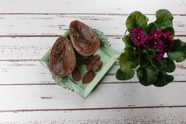 Two halves of chocolate Easter egg, on a small old tray. Next to mini chocolates and flowers.