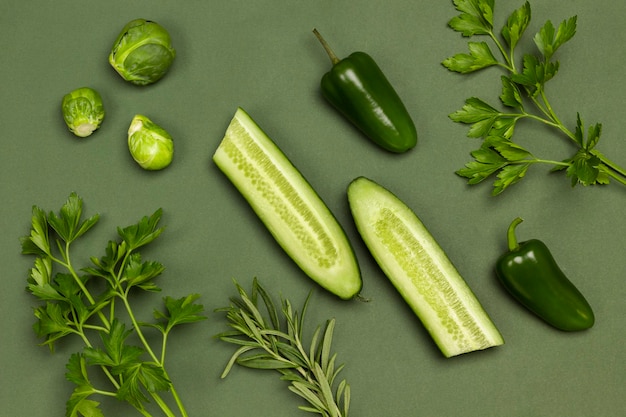 Две половинки огурца, брокколи, перец и веточки петрушки. Зеленые овощи на зеленом фоне. Плоская планировка