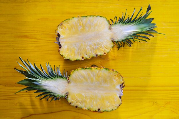 Two halves of pineapple ananas on yellow table. Top view