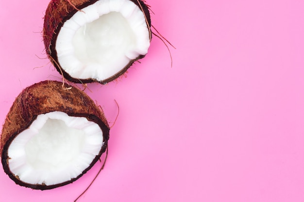 Two halves of a ripe coconut on a pink background