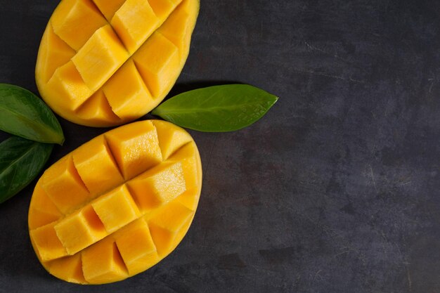 The two halves of ripe mango on the black textured table View from above Copy space