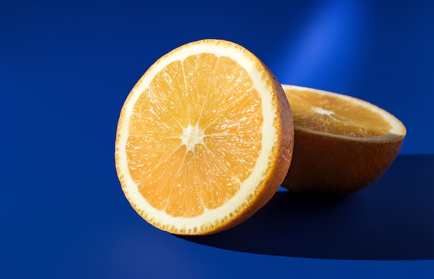Две половинки спелого апельсина на синем фоне при ярком солнечном свете.