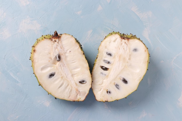 Two halves of ripe soursop on light blue background top view