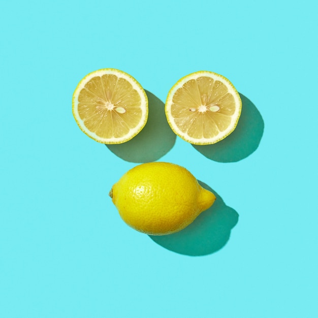 Two halves and a whole ripe lemon in the shape of a face with shadow reflection on a blue background