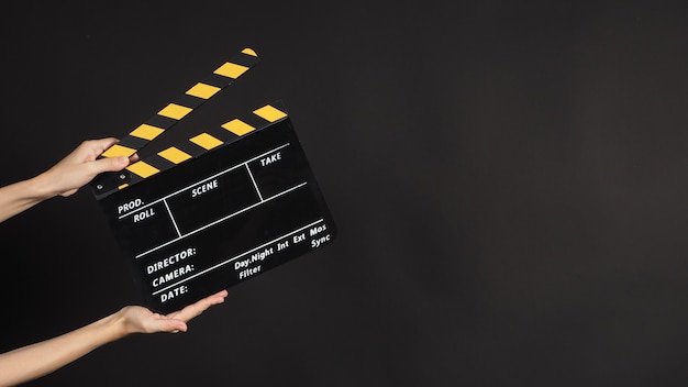 Two Hand's holding yellow&amp;black Clapperboard or movie slate use in video production and cinema industry on black background.