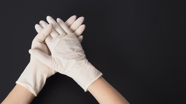 Two hand wear white latex gloves and hold hands on black background.