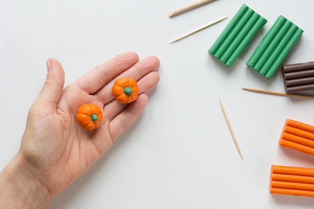 Two handmade small pumpkins made from polymer clay on woman\
hand on the white background