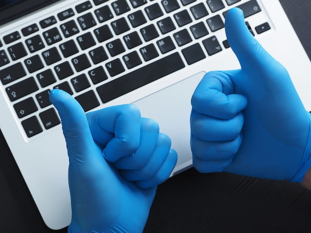 Two hands in blue gloves showing thumbs up, Portable laptop.