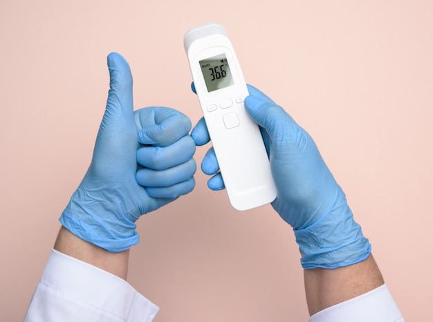 Due mani in guanti di lattice blu tengono un termometro elettronico per misurare la temperatura, dispositivo senza contatto