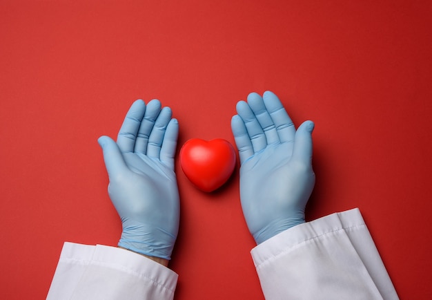 Due mani in guanti di lattice blu che tengono un cuore rosso, concetto di donazione, vista dall'alto