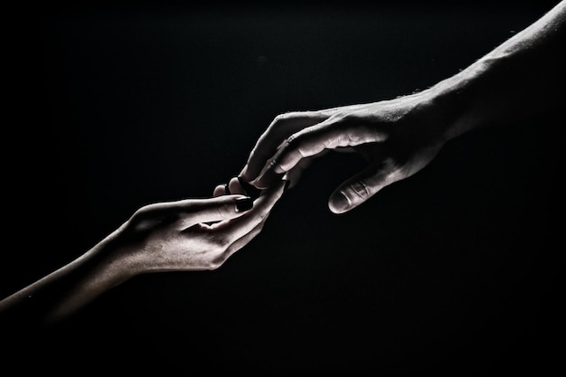 両手友達に手を差し伸べる救助または手のしぐさを助ける救いの概念救助時の二人の手は黒い背景に孤立している優しさテンデットタッチ