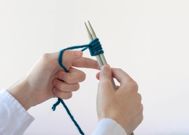 Two hands hold yarn and knitting needles and type loops.