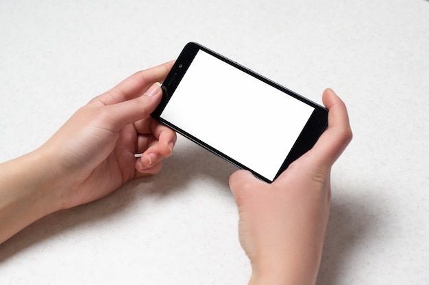 Two hands holding black phone on white wall