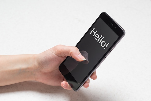 Photo two hands holding black phone with the inscription hello on white wall