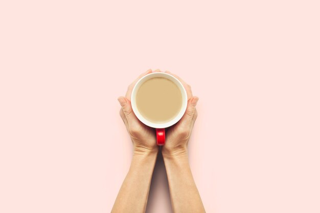 Photo two hands holding a cup with hot coffee on a pink background. breakfast concept with coffee or tea. good morning, night, insomnia. flat lay, top view