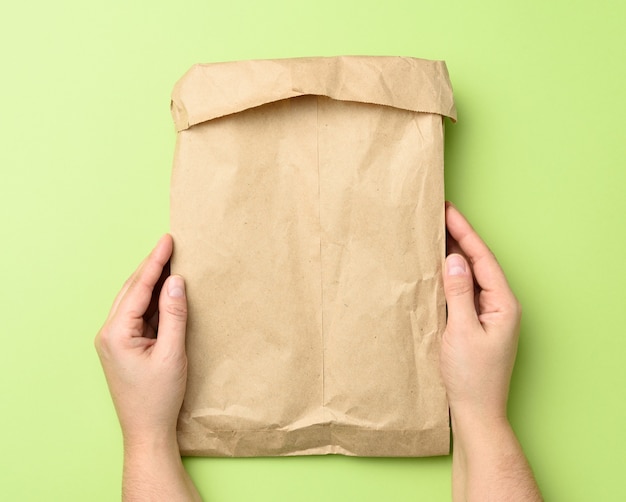 Две руки держат бумажный пакет из коричневой крафт-бумаги на зеленом