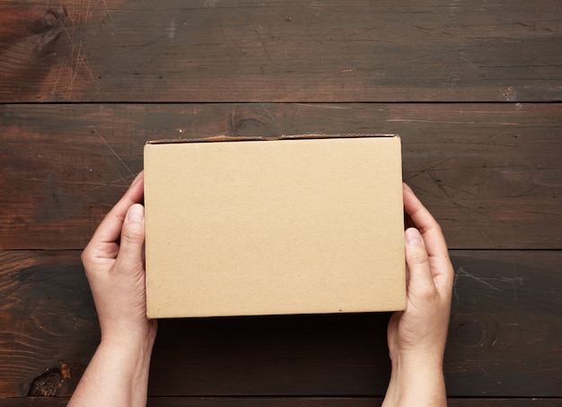 Two hands holding a rectangular cardboard box of brown kraft paper