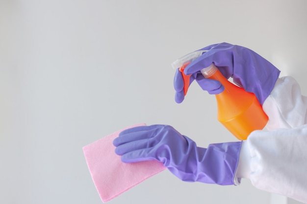 Two hands in rubber gloves, one holding a surface treatment cloth, the other an orange spray bottle