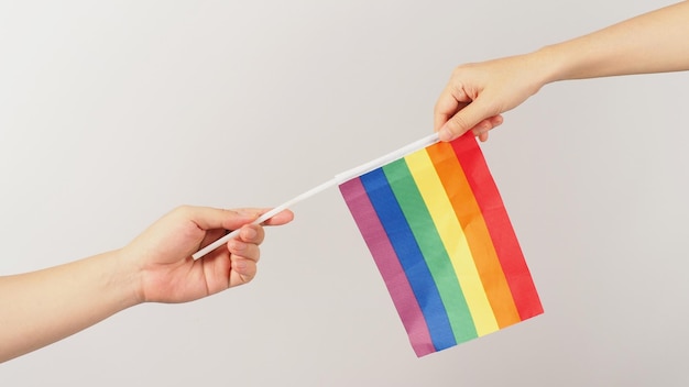 Two hands send and receive a rainbow flag on white background LGBT CONCEPT