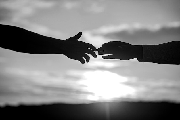 Two hands silhouette on sky background connection or help concept Black and white