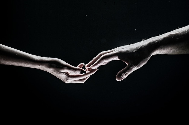 Two hands stretch each other black background Couple in love holding hads close up Helping hand support friendship