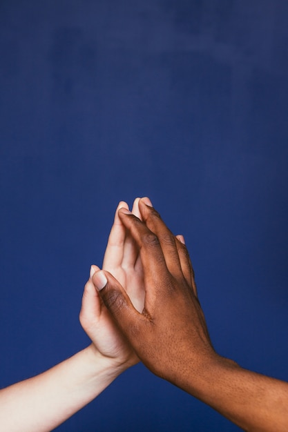 Two hands, white and black race contrast, fingertips touch on violet scene with free space for text, closeup