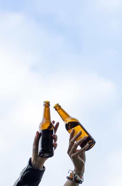 Two hands with two drinks in the air Female hands lifting two bottles of beer in the air Close up of hands celebrating with beer bottles in the air