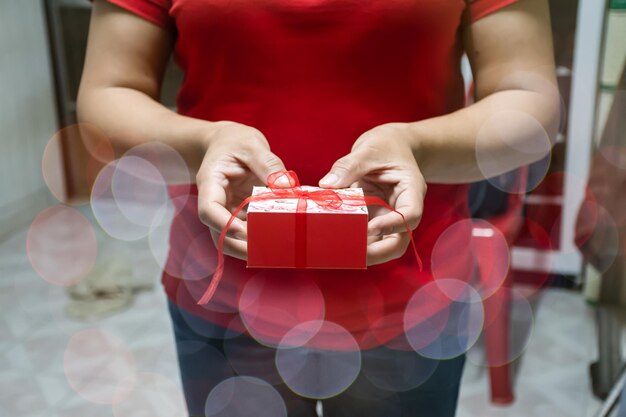 The two hands of women holding and receive red color Presents celebrates box with red ribbons on Christmas day take closeup photography image is a landscape with blurred background