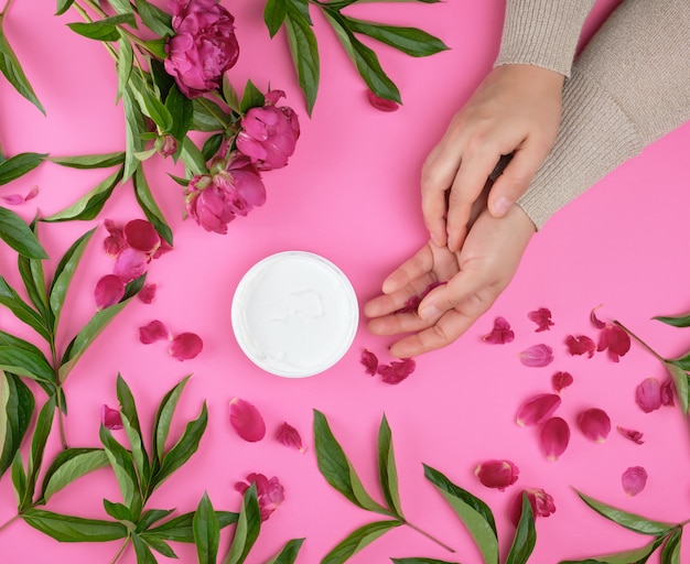 Two hands of a young girl with smooth skin and a jar with thick cream 