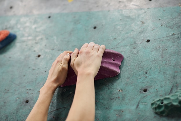 Две руки молодой спортсменки хватаются за одну из искусственных скал на альпинистском снаряжении во время тренировки