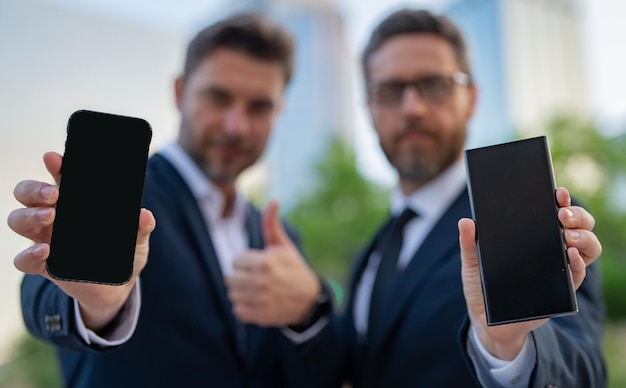 Two handsome businessman using phone and standing on the street outdoor portrait of a serious