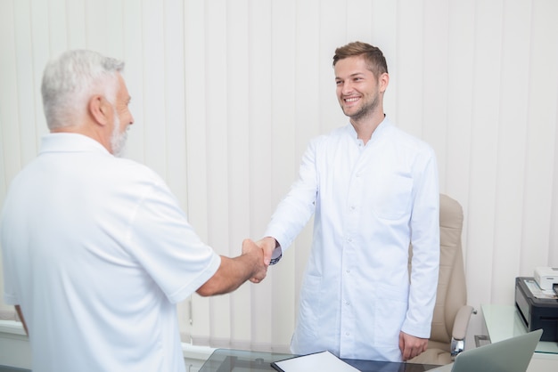 Two handsome doctors shaking hands in light cabinet.