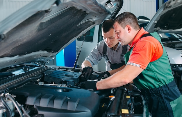 Two handsome mechanics in uniform are working in auto service