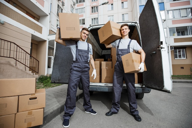 Two handsome workers wearing uniforms are standing in front of the van full of boxes