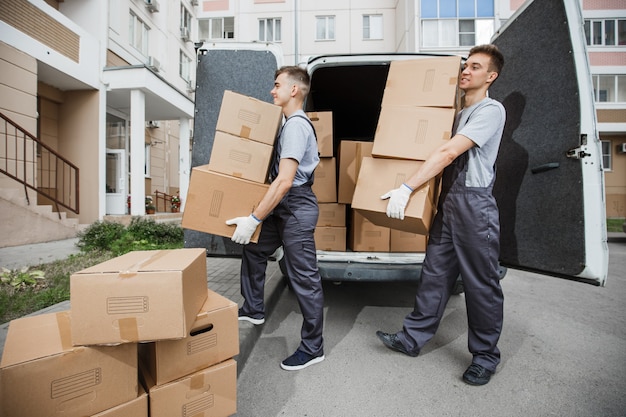 Фото Два красивых рабочих в форме разгружают фургон, полный коробок.