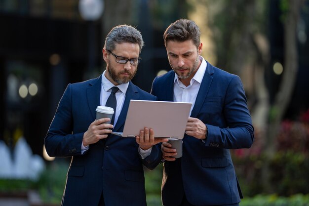 Two handsome young businessmen in classic suits using laptop handsome business man in suits working