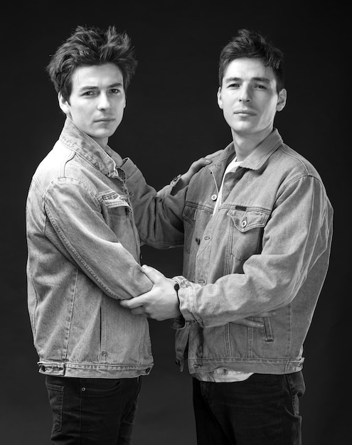 Two handsome young men posing on a black background. Two brothers