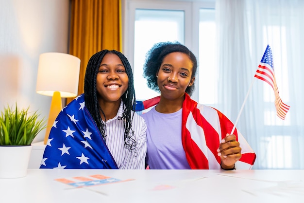 Two happy african american sister celebrating usa independence day at home in cozy apartment