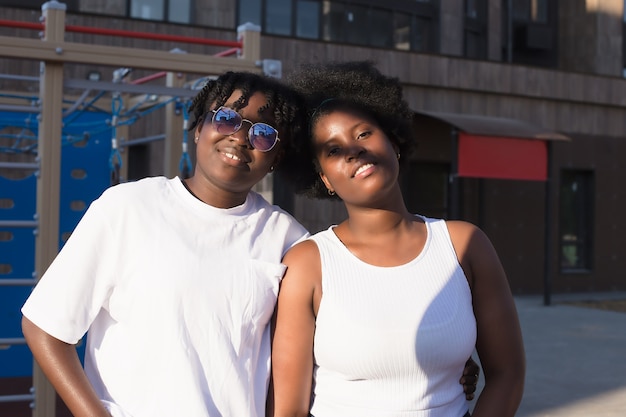 Two happy African-American women communicate and laugh on the street in the summer.