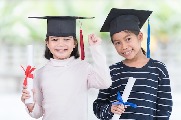 Two happy Asian female school kid graduates with a graduation cap holds a rolled certificate. Graduation Celebration Concept Stock Photo