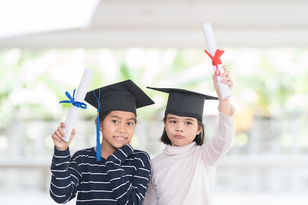 Two happy Asian female school kid graduates with a graduation cap holds a rolled certificate. Graduation Celebration Concept Stock Photo