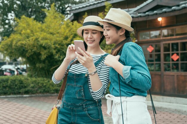 사진 화창한 거리 공원에서 인터넷으로 다음 관광지에 대해 논의하는 스마트 폰을 공유하는 두 명의 행복한 매력적인 여성 친구. 여행하는 동안 휴대전화로 온라인 지도를 함께 보고 있는 웃는 소녀들