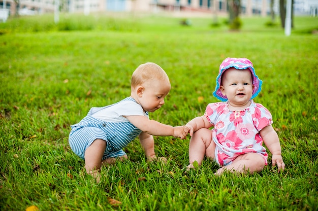 Two happy baby boy and a girl age 9 months old, sitting on the grass and interact, talk, look at each other.