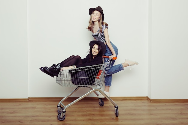 Two happy beautiful teen women  driving shopping cart indoors