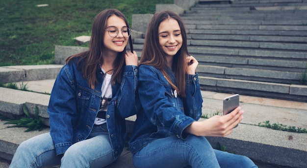 Photo two happy best friends using social media on their smartphones