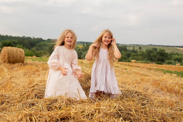 two happy blonde girls with long hair in linen dresses throw hay