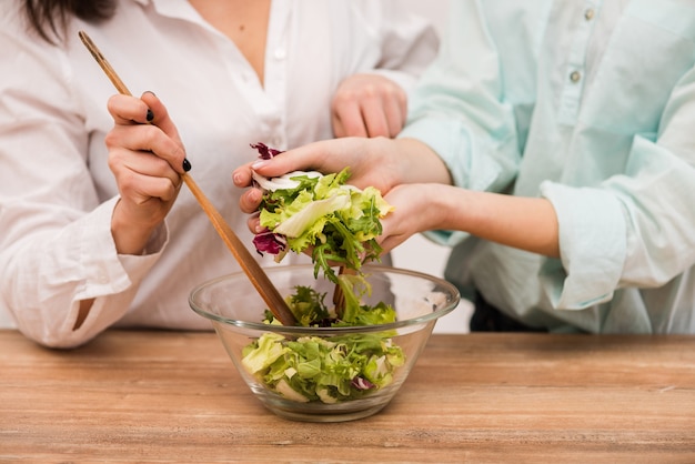 Two happy brunette girls cooking fresh salad together, close-up