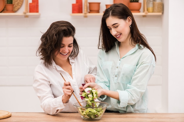 Two happy brunette girls cooking fresh salad together